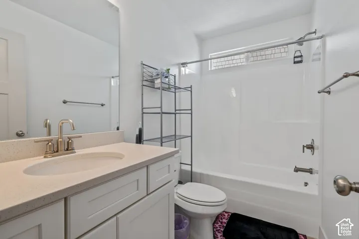 Bathroom featuring a white vanity with a composite countertop and integrated oval sink, full-width mirror, and a tub-shower combination with chrome fixtures and an elongated transom window