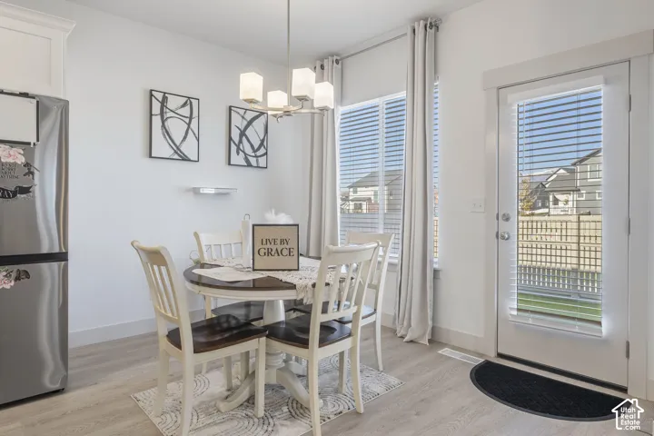 Dining area featuring light wood-finish flooring, a multi-bulb chandelier, large windows with horizontal blinds, and a glass-paneled exterior door