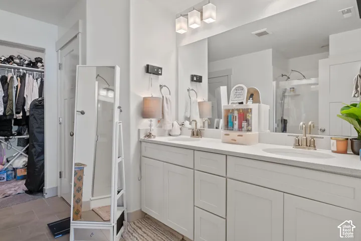 Dual-sink vanity with white shaker-style cabinetry, solid-surface countertop, widespread metal faucets, and large wall-mounted mirror