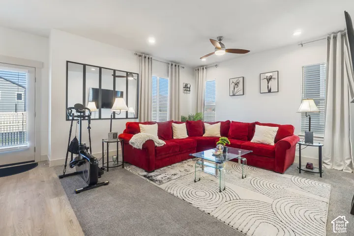 Living area featuring recessed lighting, a modern ceiling fan with wood-finish blades, large windows with neutral window treatments, a decorative metal-framed wall mirror, and wood-finish flooring