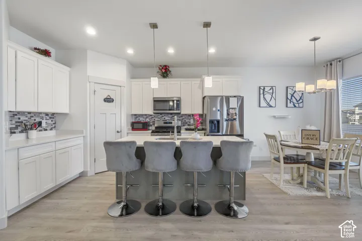 Kitchen featuring white cabinetry, center island with stone countertop, stainless steel appliances, mosaic tile backsplash, and wood-finish flooring