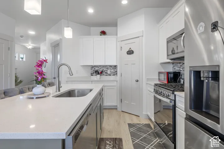 Kitchen featuring white cabinetry, quartz countertops, a central island with an undermount stainless steel sink, tile backsplash, and stainless steel appliances