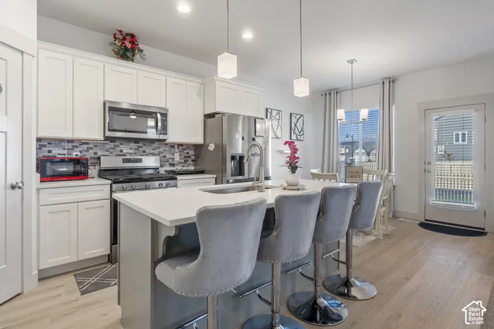 Kitchen featuring white shaker-style cabinetry, quartz countertops, a multi-tone tile backsplash, stainless steel appliances, and a center island with a built-in sink