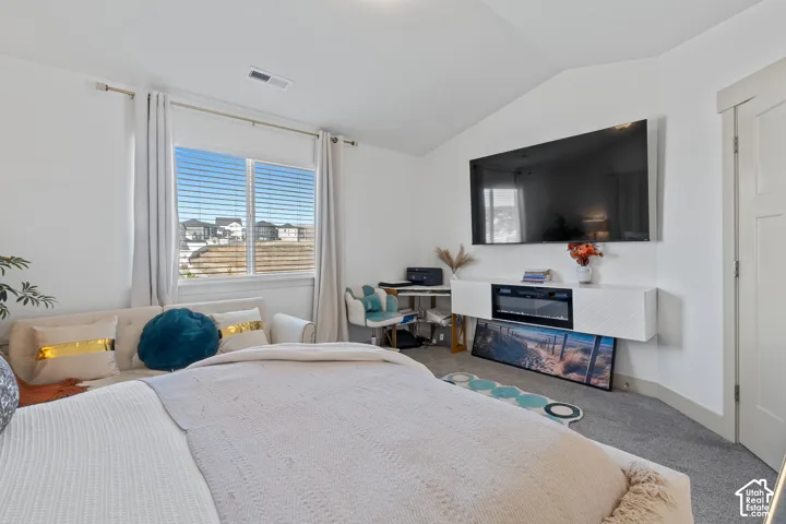 Vaulted ceiling, wall-mounted electric fireplace, built-in cabinetry, and neutral carpeting