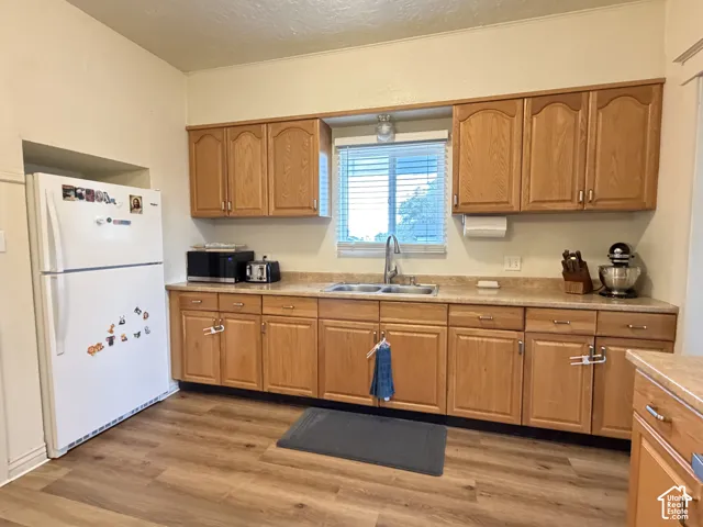 Kitchen featuring wood cabinetry, laminate countertops, double-basin stainless steel sink with a high-arch faucet, and wood-finish flooring