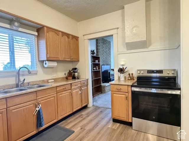 Kitchen featuring wood cabinetry, stone-finish countertops, stainless steel range with overhead vent hood, dual-basin stainless steel sink with pull-down faucet, and wood-finish flooring