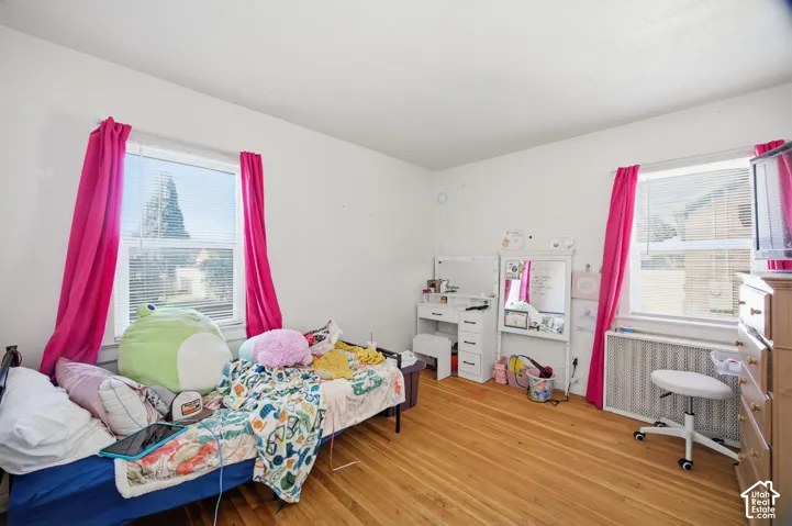 Bedroom featuring wood-finish flooring, dual windows with integrated blinds, and a metal radiator cover