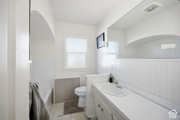 Bathroom featuring beadboard wainscoting, an arched alcove over the bathtub, a full-width vanity mirror, and an integrated basin