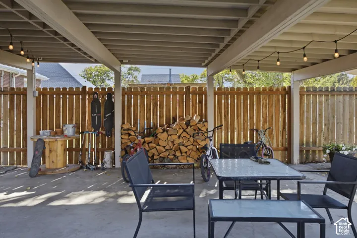 Covered concrete patio featuring an exposed-beam ceiling and string lighting, enclosed by a vertical wood privacy fence