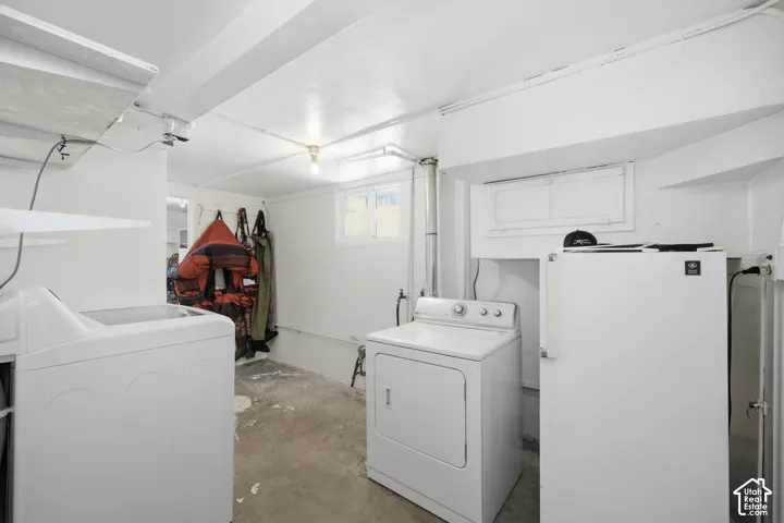 Utility area featuring concrete flooring, white painted walls, natural light access via a horizontal window, and dedicated laundry hookups