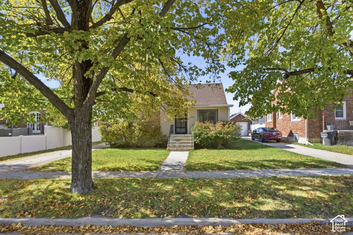 Single-story residence featuring a front porch with stairs, concrete walkway, detached garage, and mature trees