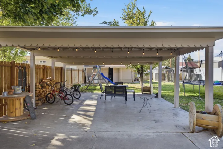 Covered outdoor patio featuring a concrete foundation, scalloped trim, and built-in string lighting, enclosed by a wood privacy fence