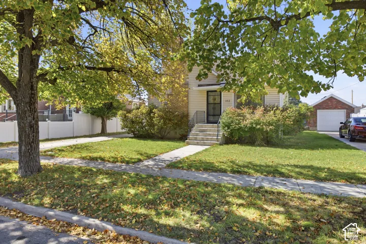Siding exterior featuring a front staircase with iron railings, mature landscaping, white privacy fencing, and a detached garage