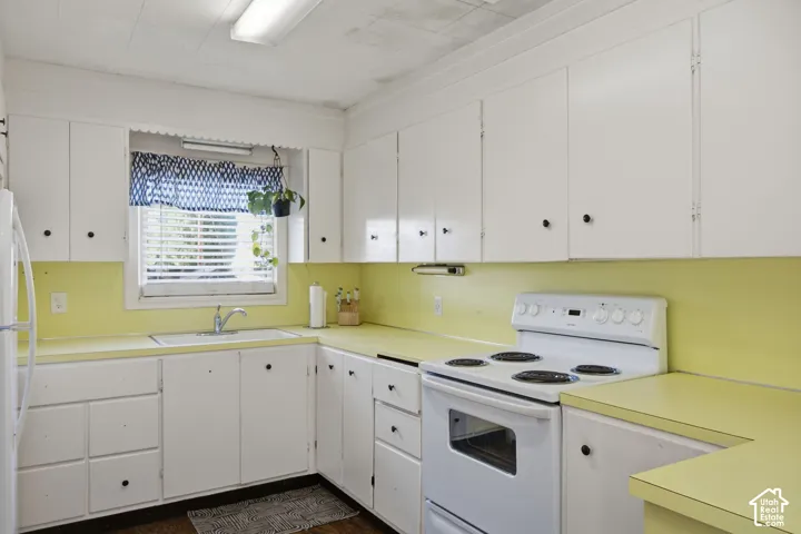 Kitchen featuring white cabinetry, laminate countertops, a dual-basin sink with a metal faucet, and a white electric range
