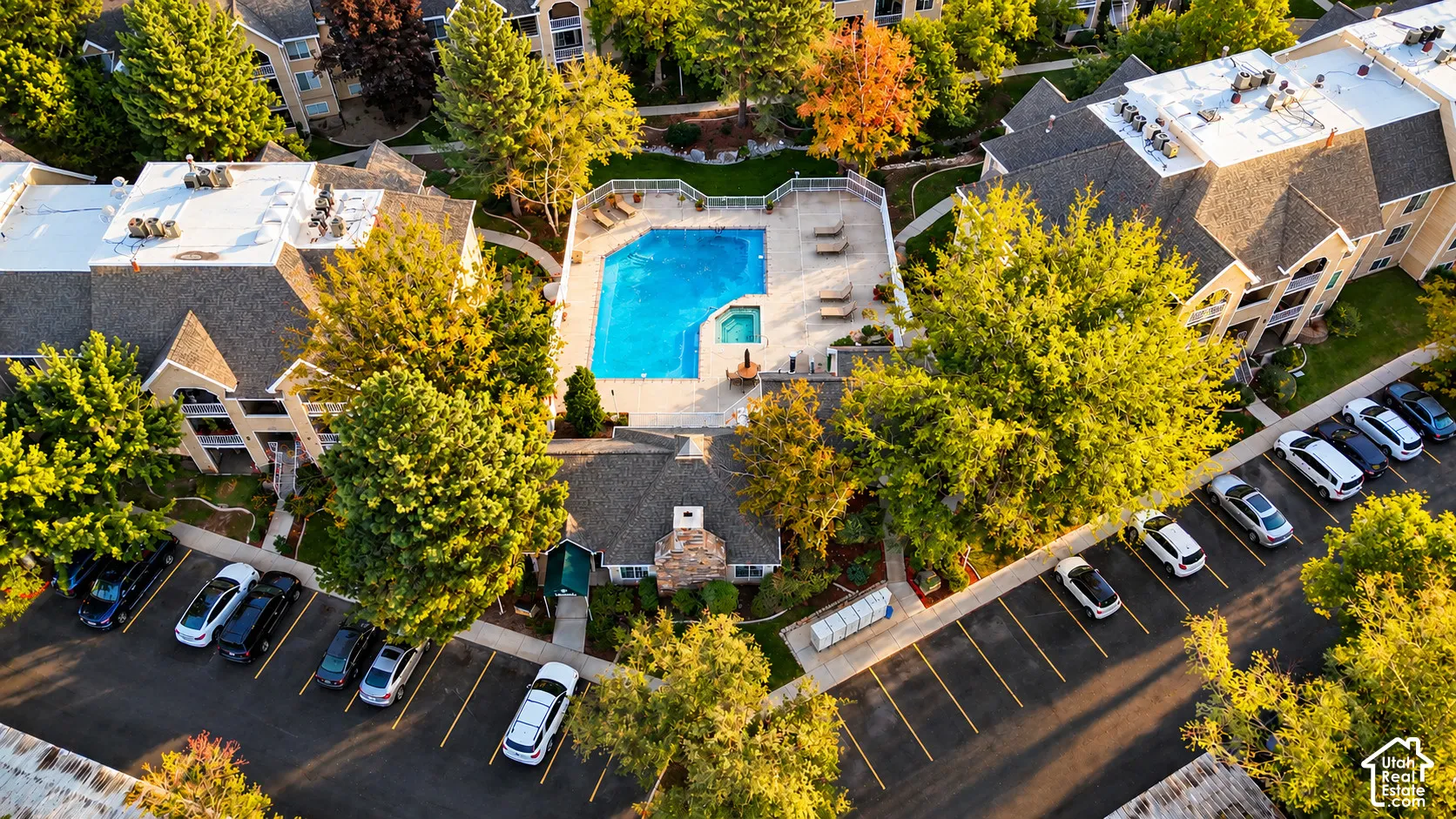 Aerial perspective of multi-family residential complex featuring a swimming pool, attached hot tub, paved parking areas, and mature landscaping