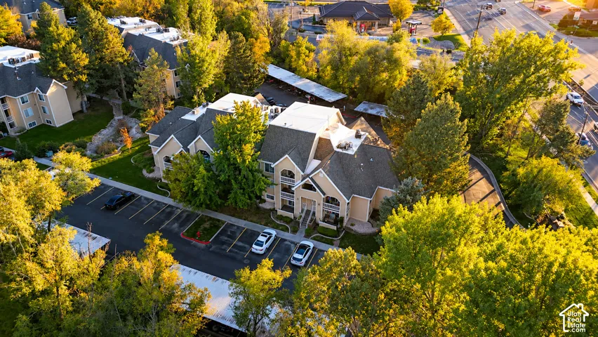 Aerial perspective featuring multi-story structures with pitched shingle roofing, paved surface parking lots, covered parking structures, and mature deciduous trees
