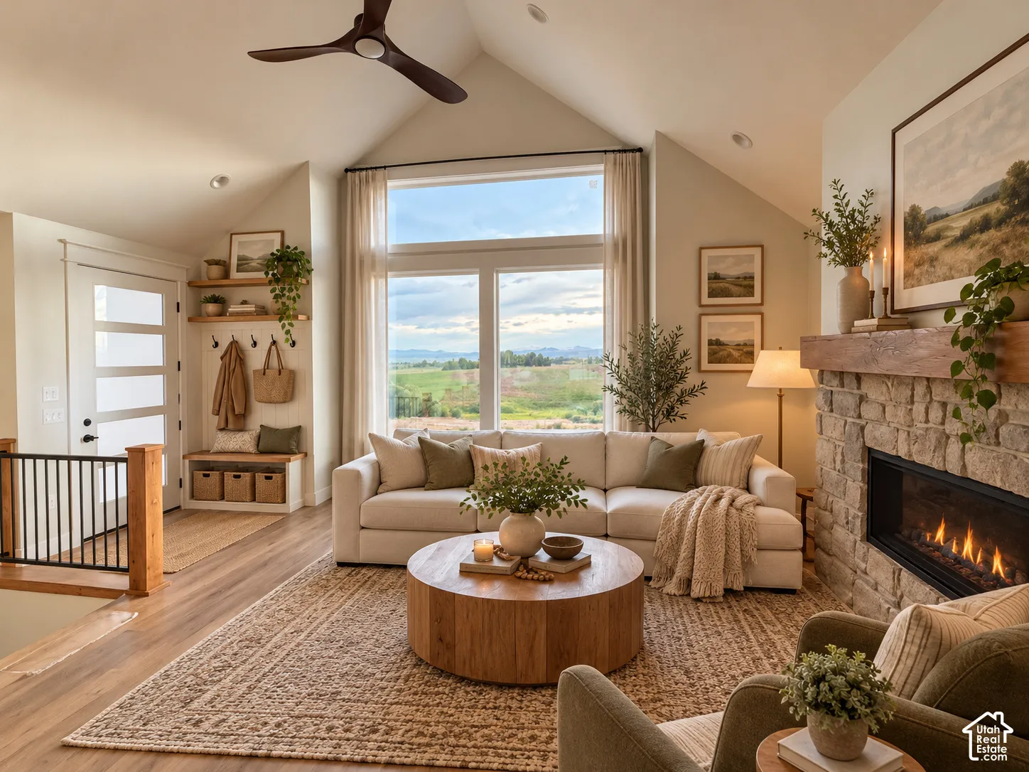 Vaulted ceilings featuring a dark wood-finish ceiling fan, natural stone fireplace with a thick timber mantel, & large multi-pane windows.