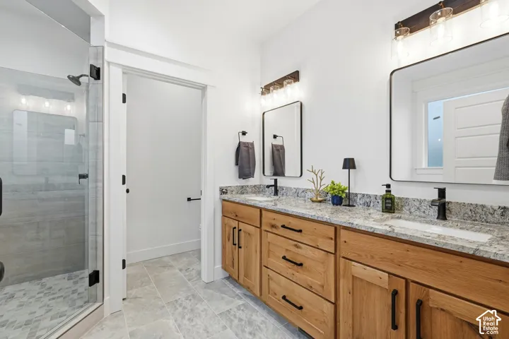 Bathroom featuring a dual-sink vanity with wood-finish cabinetry, stone countertops, matte black fixtures, and a walk-in glass-enclosed shower with tile flooring
