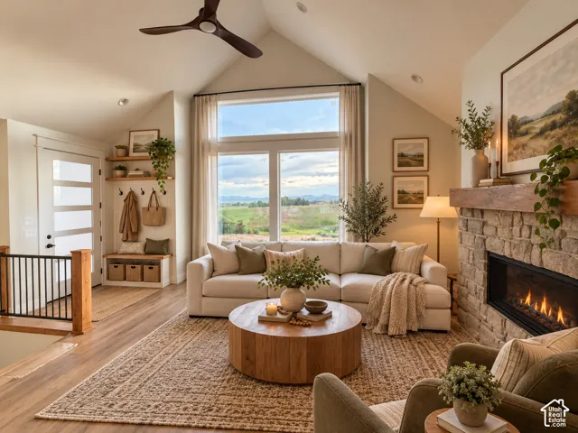 Vaulted ceilings featuring a dark wood-finish ceiling fan, natural stone fireplace with a thick timber mantel, & large multi-pane windows.
