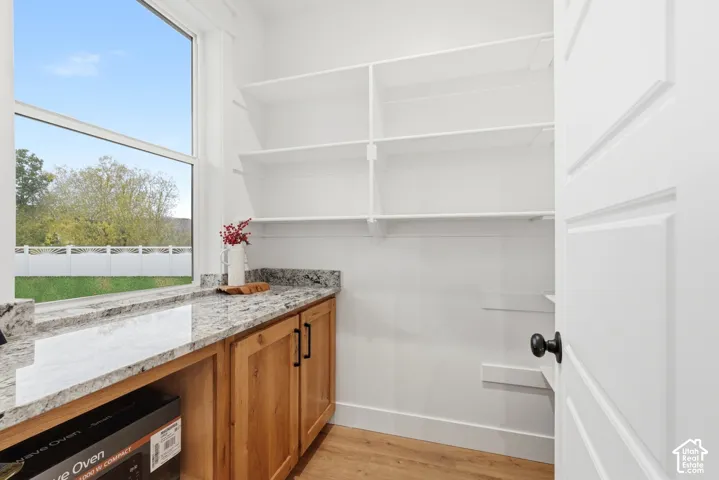 Storage area featuring multi-level open shelving, stone-finish countertops, wood-finish cabinetry, and a large window