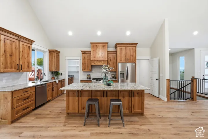Kitchen featuring stained wood cabinetry, stone countertops, a large center island, recessed lighting, and wood-finish flooring under a vaulted ceiling