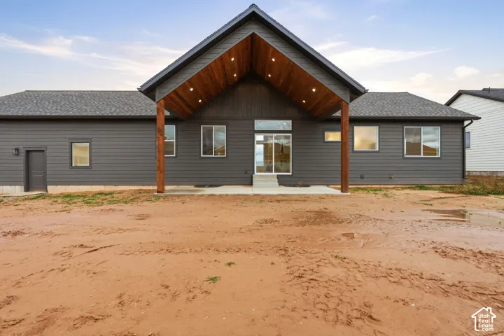 Exterior featuring dark horizontal siding, a gabled roofline with wood-finished soffits, recessed lighting, exposed timber support columns, and a concrete patio