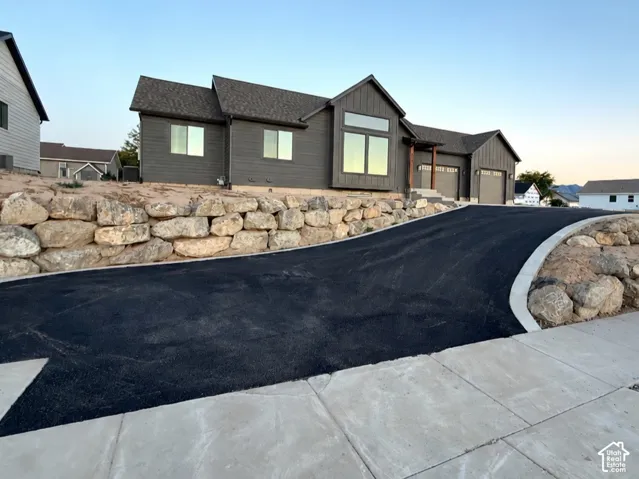 Modern exterior featuring dark siding, asphalt driveway, concrete curbing, tiered natural stone retaining walls, and mountain scenery