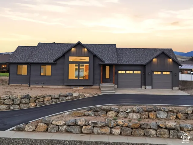 Exterior facade featuring dark horizontal siding, asphalt shingle roofing, multi-car garage, and terraced stone retaining walls lining the paved driveway