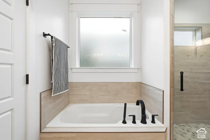 Soaking tub with a matte black faucet and handheld sprayer, surrounded by neutral-toned tile wainscoting and topped with a square window
