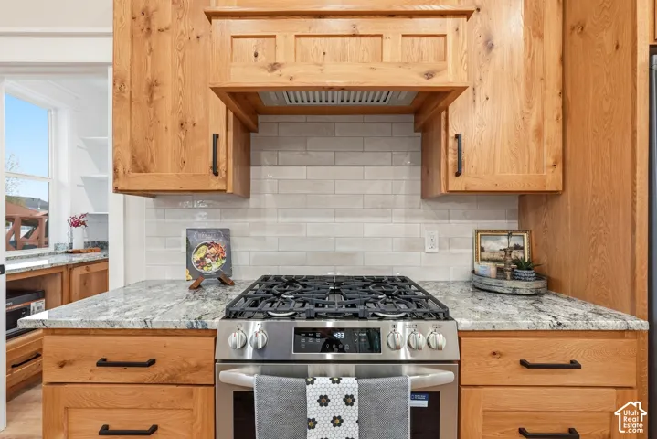 Custom wood cabinetry, stainless steel gas range, stone countertops, subway tile backsplash, and built-in wooden range hood