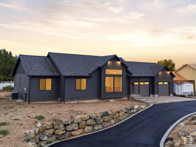 Dark-tone horizontal siding exterior featuring a multi-gabled roofline, tiered stone retaining wall, paved driveway, and attached multi-car garage