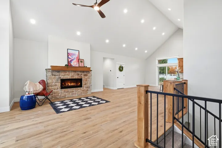 Vaulted ceiling featuring recessed lighting and a ceiling fan, stone-surround fireplace with a wood mantel, and wood-finish flooring with a metal-railing staircase