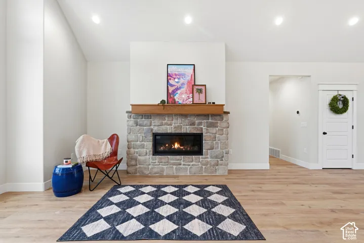 Stone fireplace featuring a natural stone facade, recessed firebox, and wood mantel, finished with recessed ceiling lighting and wood-finish flooring