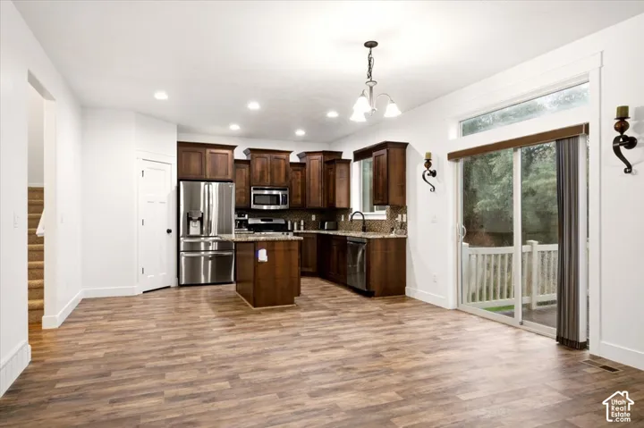 Kitchen featuring stained wood cabinetry, stainless steel appliances, a center island, wood-finish flooring, and sliding glass doors