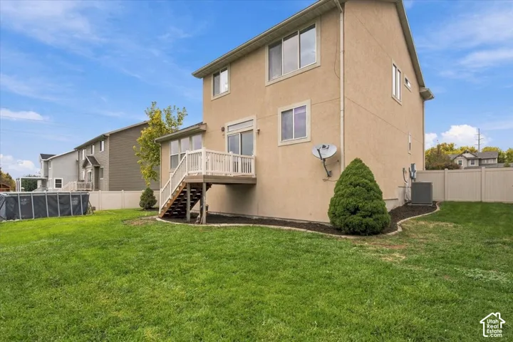 Multi-level exterior featuring a stucco facade, an elevated wooden deck with stairs, a vinyl perimeter fence, and a grass-covered backyard