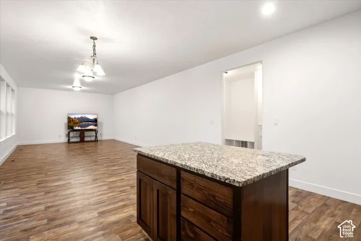 Kitchen island featuring dark wood cabinetry and a stone countertop, complemented by wood-finish flooring and a multi-bulb hanging light fixture