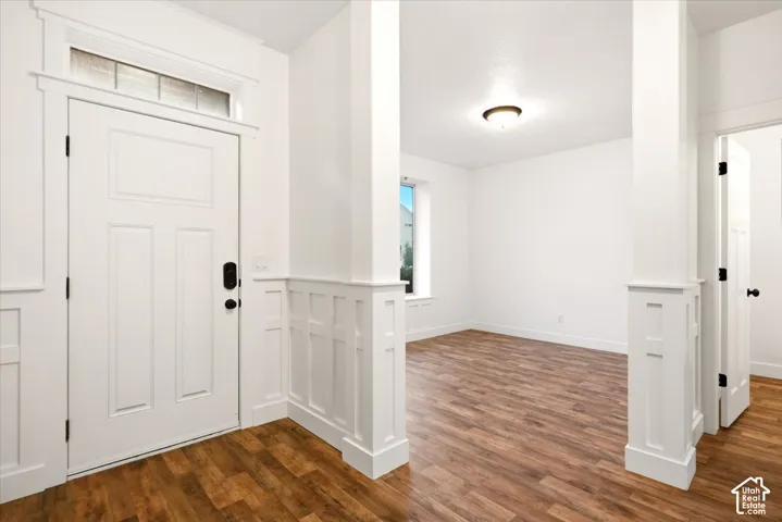 Entryway featuring white paneled wainscoting, wood-finish flooring, a transom window above the door, and structural pillars