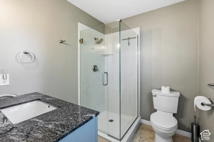 Bathroom featuring a stone countertop with an integrated undermount sink, a glass-enclosed shower with a wall-mounted showerhead, and neutral wall tones