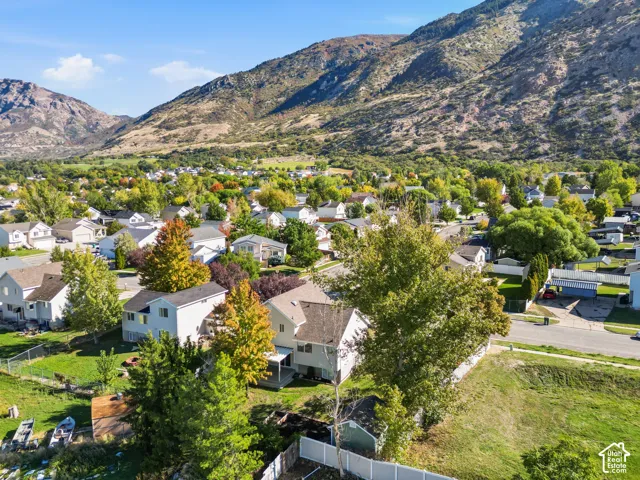 Aerial perspective of residential property featuring a multi-level residence, expansive lot with mature trees, established landscaping, and a prominent mountain backdrop