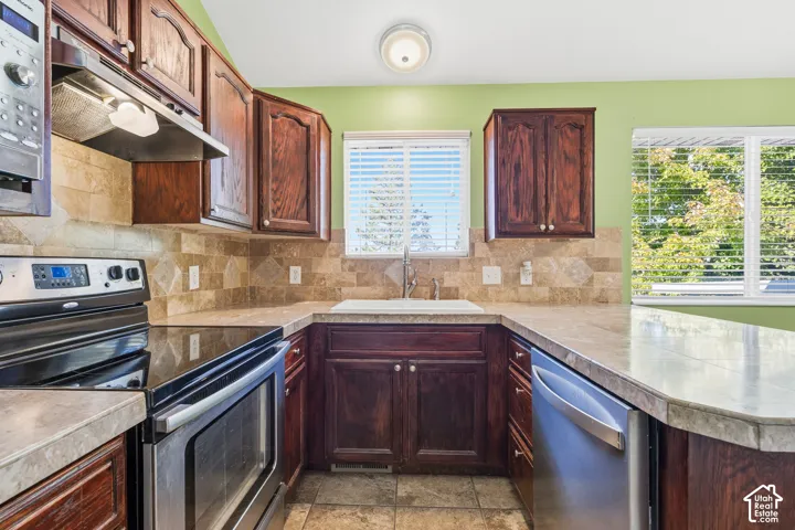 Kitchen featuring dark wood cabinetry, stone-finish countertops, tiled backsplash, stainless steel appliances, and tile flooring
