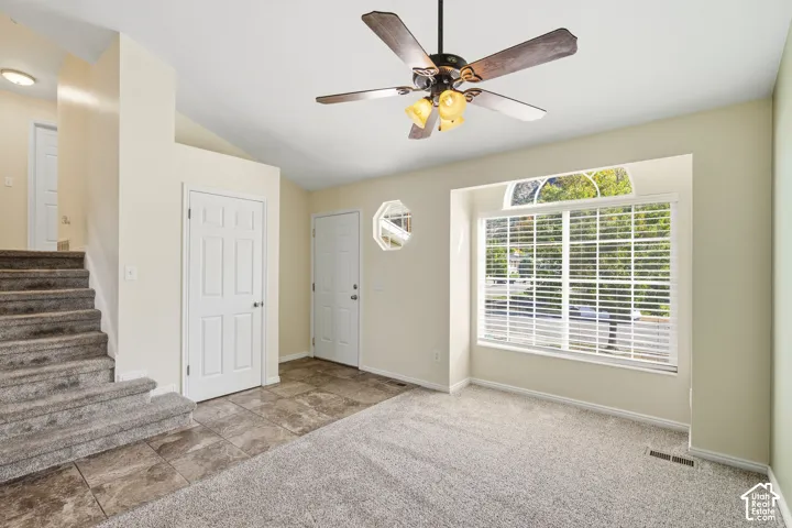 Vaulted ceilings featuring a multi-blade ceiling fan, large window with a semicircular transom, octagonal accent window, and tile flooring