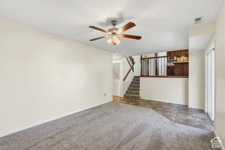 Living area featuring wall-to-wall carpeting, ceiling fan with integrated lighting, tile flooring, staircase with wood railings, and glass sliding door