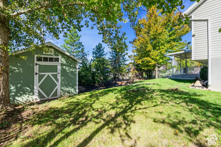 Backyard space featuring a green storage shed with transom window detailing, a covered porch with metal railing, and raised garden beds