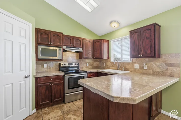 Kitchen featuring dark-finish wood cabinetry, stone-style countertops, tiled backsplash, stainless steel appliances, and vaulted ceiling