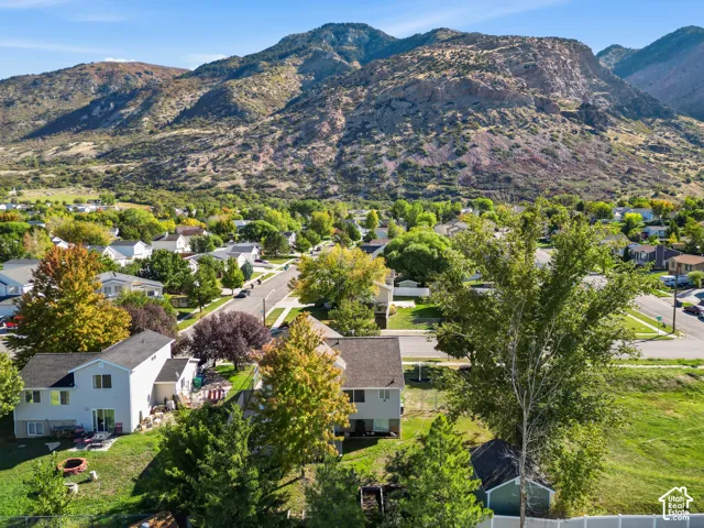 Aerial perspective featuring prominent mountain terrain, mature trees, multi-level residential structures, and expansive green space