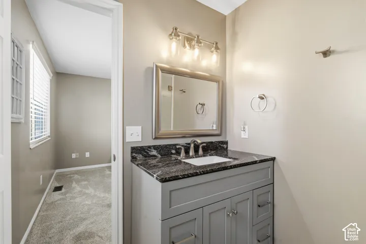 Gray vanity cabinet featuring a dark stone countertop, integrated sink with a metal faucet, framed wall mirror, and three-bulb vanity light fixture