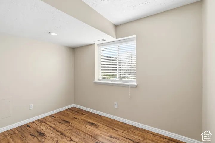 Room featuring wood-finish flooring, recessed lighting, and a single-pane window with horizontal blinds