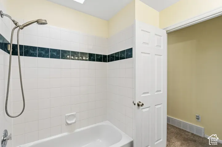 Bathroom featuring a white tile surround with a decorative dark stone-finish accent border, a standard soaking tub, a multi-setting hand-held shower head, and a six-panel interior door