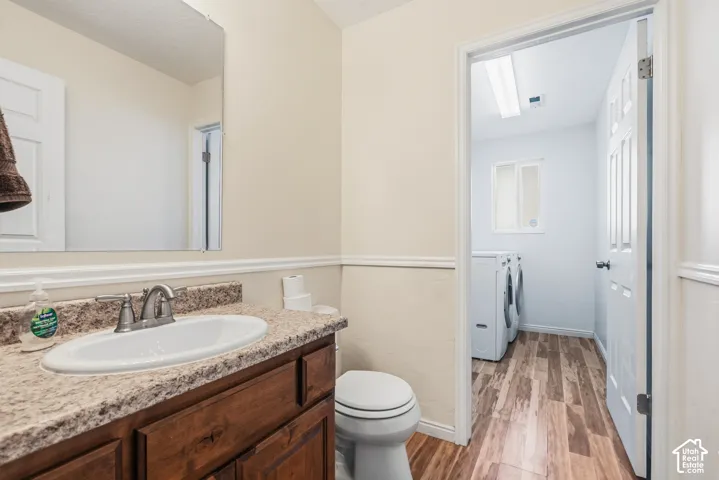 Bathroom featuring a wood-finish vanity with a stone-composite countertop, an undermount sink, a wall-mounted mirror, and wood-finish flooring