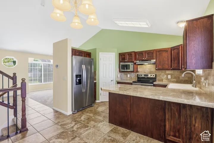 Kitchen featuring wood cabinetry, stone-finish countertops, stainless steel appliances, tile flooring, and vaulted ceilings